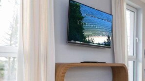 Ein modernes Zimmer mit an der Wand befestigtem Fernseher, einem Holzstuhl und einem Glastisch.