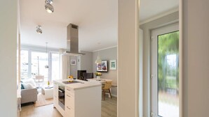 Una cocina moderna con una isla central, horno empotrado y campana de acero inoxidable. Hay una zona de comedor con mesa y sillas, y un ventanal que proporciona luz natural.