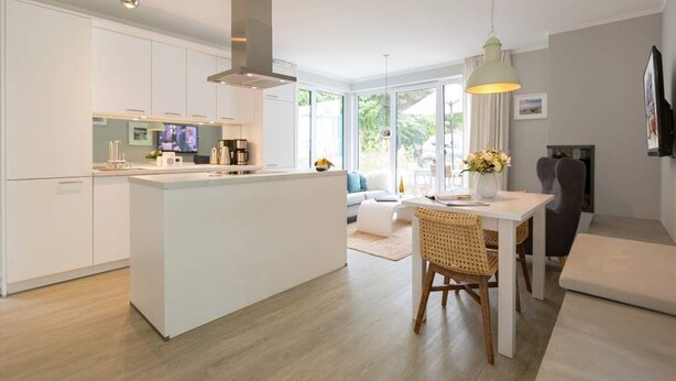 Una cocina moderna con armarios blancos, una isla central y un comedor con mesa y sillas.
