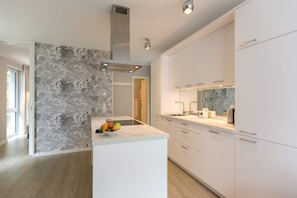 A modern kitchen with white cabinets, a marble island, and a stone accent wall. - Villa Bellevue, App. 09 Garden house (Heringsdorf)