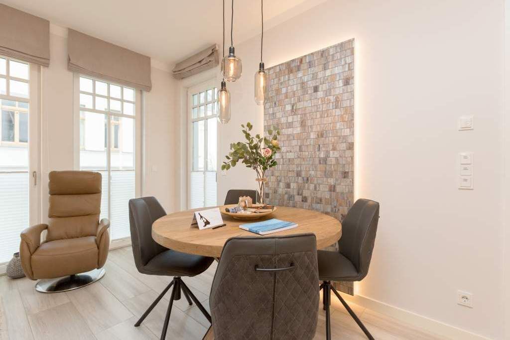 Un espace repas moderne avec une table ronde, quatre chaises, un fauteuil en cuir marron, un vase avec des fleurs et un mur à texture.