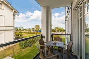 Un balcone con sedie in vimini, un tavolo e vista su un giardino curato e edifici in lontananza.
