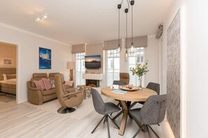 Una sala moderna con sofá, sillón, mesa de comedor y sillas. Hay una chimenea, un televisor y obras de arte en las paredes.
