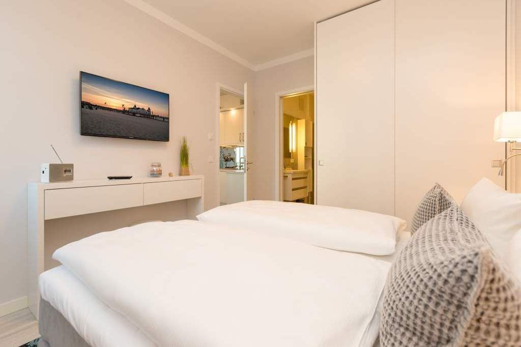 Ein Hotelzimmer mit zwei Betten, einem wandmontierten Flachbildfernseher, einem Nachttisch mit Lampe und Blick auf den Flur.