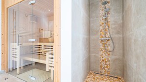 A modern bathroom with a glass shower enclosure, a wooden bench, and a tiled floor.