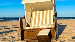 A beach chair with a striped cushion and a white canopy, positioned on a sandy beach with the ocean in the background.