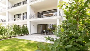 A multi-story building with balconies, a patio area with outdoor furniture, and a well-maintained garden.