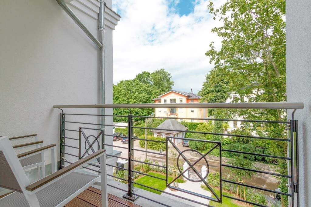 A balcony with a metal railing, a white chair, and a view of a residential area with houses and trees.