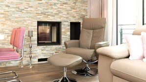 Una habitación moderna con pared de piedra, chimenea, sofá color beige y sillón rosa, además de una lámpara de pie.