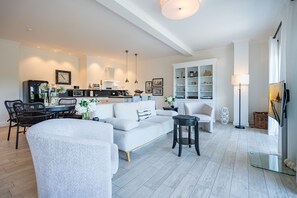 A modern living room with a sofa, dining table, chairs, and a kitchen area in the background.