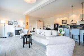 A modern living room with a fireplace, a sofa, a coffee table, and a kitchen area with a bar.