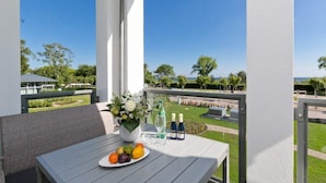 A balcony with a table set for a meal, a vase with flowers, and a view of a landscaped area.