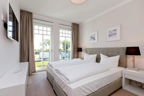 Quarto de hotel com uma cama grande, televisão na parede, escrivaninha e janela com cortinas.
