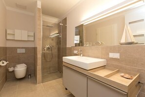 Ein modernes Badezimmer mit einem großen Spiegel, einem weißen Waschbecken, einer Duschkabine und einer Toilette.