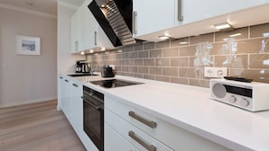 A modern kitchen with white cabinets, a built-in oven, a stove, and a radio.