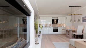A modern kitchen with white cabinets, a central island, pendant lighting, and a dining area with a table and chairs.