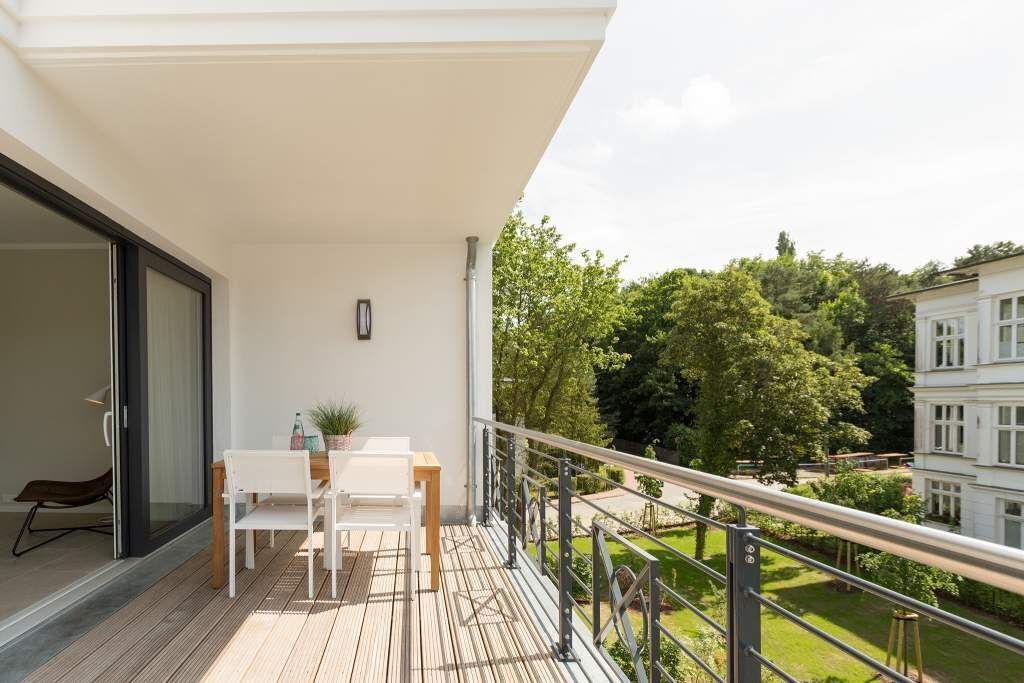 Un balcon avec une table et des chaises, un pot de fleurs et une vue sur un jardin et des bâtiments.