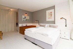 A bedroom with a large bed, a wooden side table, a nightstand, a wall-mounted lamp, and a framed picture. - Villa Strandgrün, App. 05 (Heringsdorf)