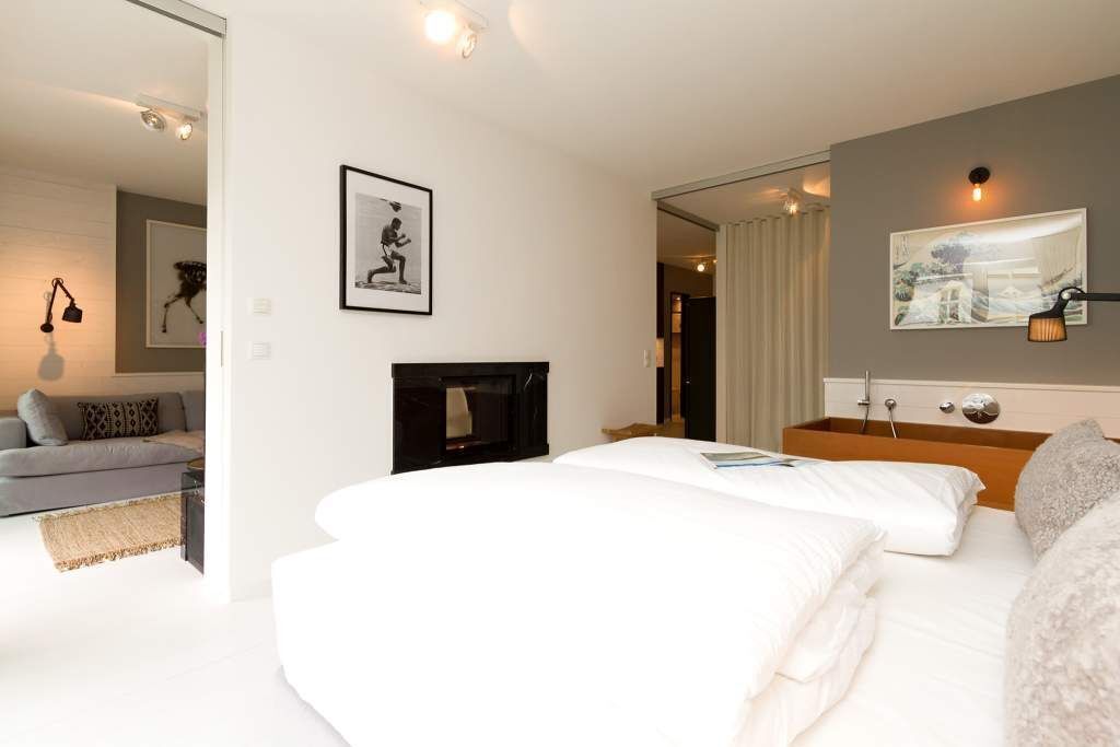 Una habitación de hotel moderna con una cama grande, un televisor de pantalla plana, una mesita de noche y un sofá en la zona de estar contigua.