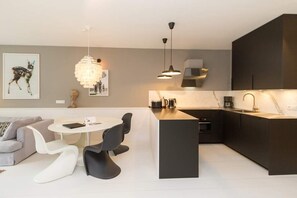A modern kitchen with a central island, pendant lighting, and a dining area with a round table and chairs. - Villa Strandgrün, App. 05 (Heringsdorf)
