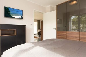Une chambre à coucher avec un lit, un téléviseur fixé au mur, une armoire et une porte donnant sur une autre pièce.