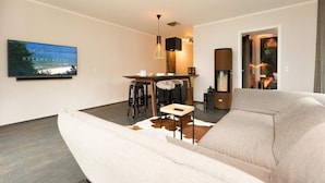 A modern living room with a sofa, a dining table with stools, a TV mounted on the wall, and a fireplace. - Villa Strandgrün, App. 06 (Heringsdorf)