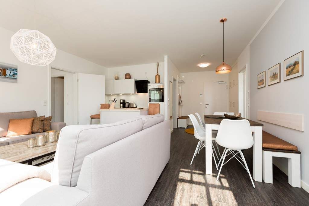 A modern kitchen with white cabinets, a built-in oven, and a dining area with white chairs and a wooden table.
