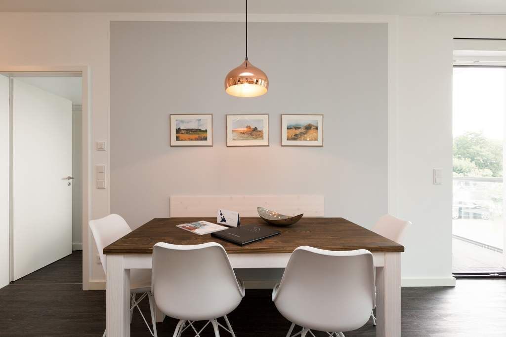 Un comedor moderno con una mesa de madera, sillas blancas, una lámpara colgante y tres cuadros en la pared.