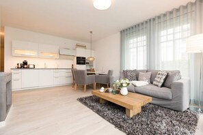 A modern living room with a grey sofa, a wooden coffee table, and a dining area with chairs and a table.