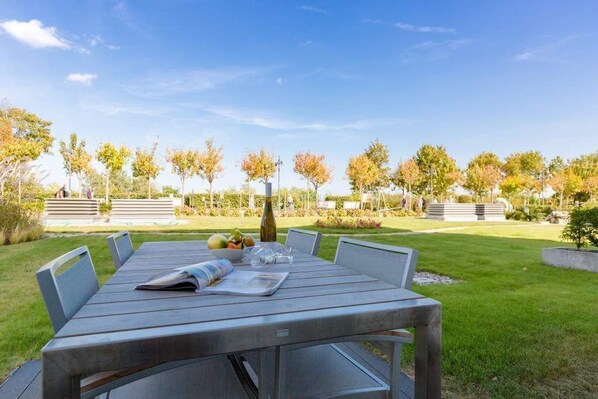 A wooden table with chairs, a bowl of fruit, and a bottle of water in an outdoor setting with a clear sky.