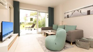 A modern living room with a sofa, a bean bag chair, a flat-screen TV, and a large window with curtains. - Villa Strandgrün, App. 02 (Heringsdorf)
