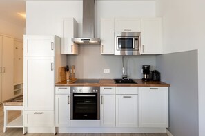 Uma cozinha moderna com armários brancos, forno embutido, micro-ondas e cafeteira.