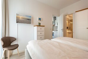 Quarto com cama, cadeira, penteadeira e vista para o banheiro.