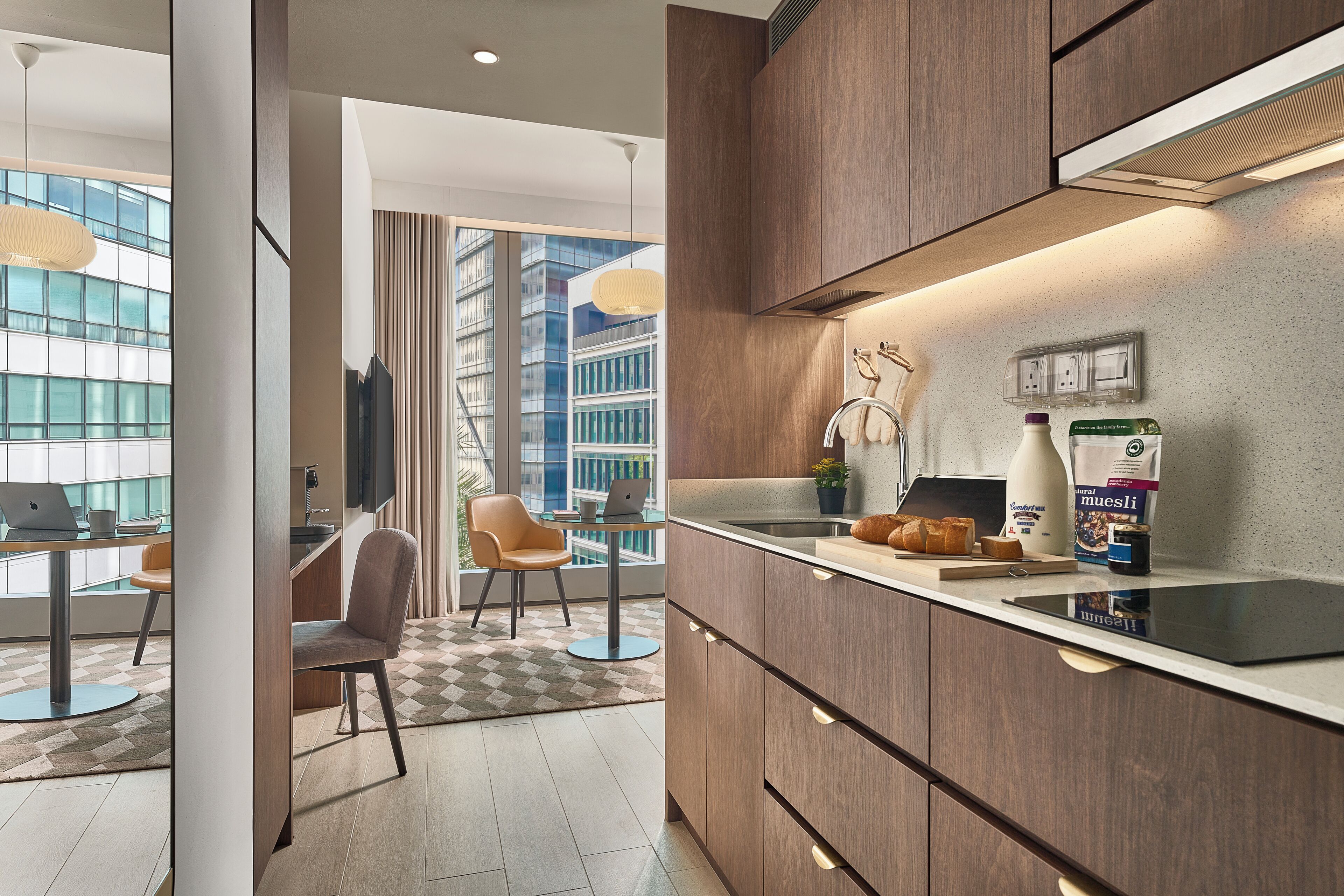Een moderne keuken met een ingebouwde kookplaat, een eethoek met een tafel en stoelen, en uitzicht op een stadsbeeld door grote ramen.