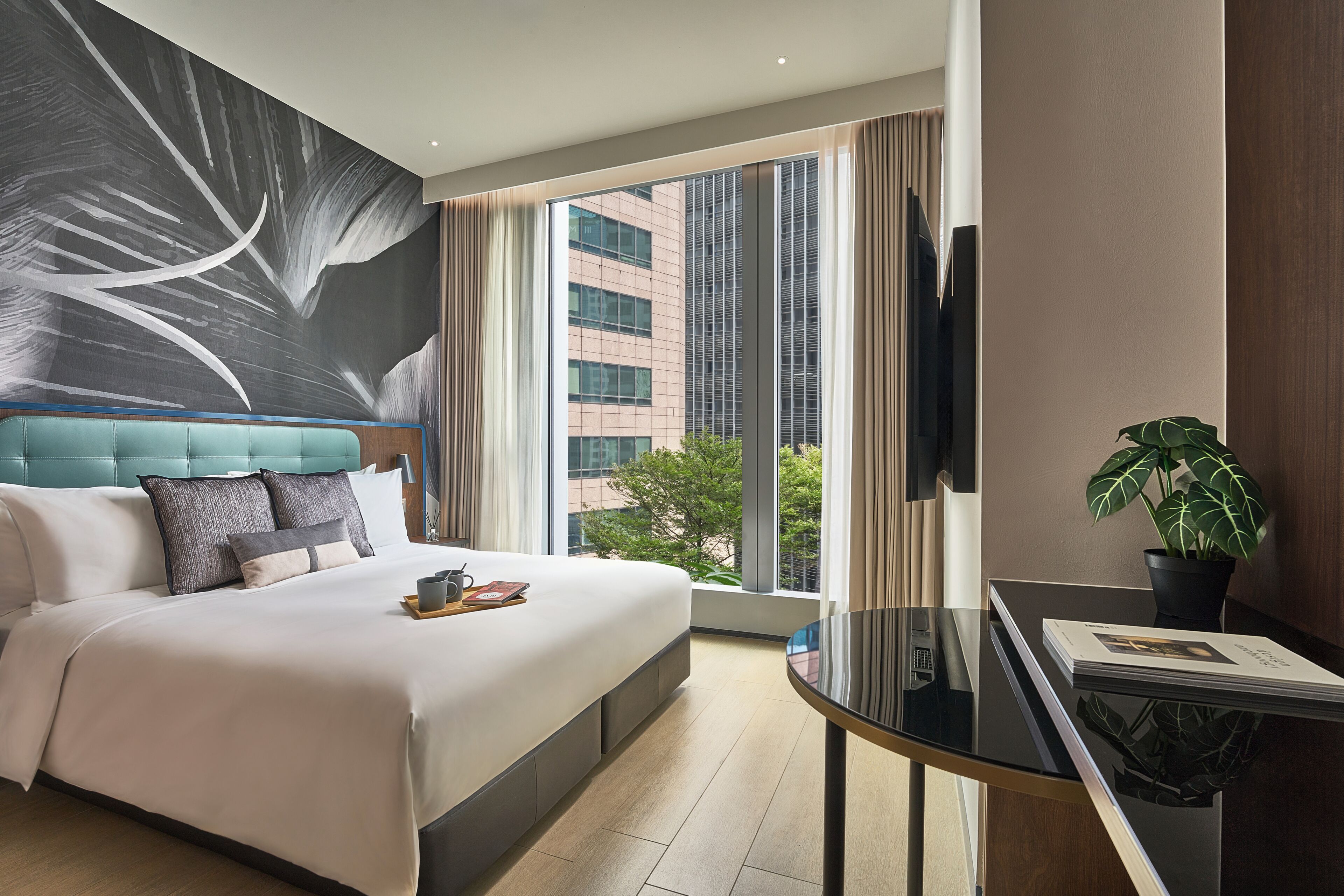 Une chambre d’hôtel avec un grand lit, un bureau, une vue sur les immeubles et une plante en pot.