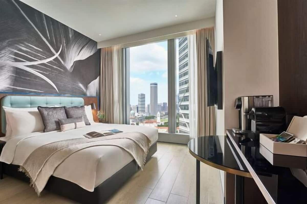 Habitación de hotel moderna con una cama grande, un escritorio, vistas de la ciudad y un cuadro abstracto de gran tamaño en la pared.
