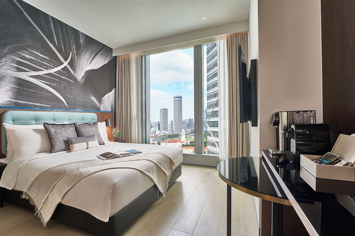 Una habitación de hotel moderna con una cama grande, un escritorio con impresora y vistas a la ciudad.