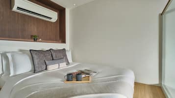 A neatly made bed with a tray of mugs, a book, and a small plant on the headboard.