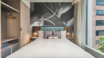 A hotel room with a large bed, a wardrobe, a nightstand, and a view of the city.
