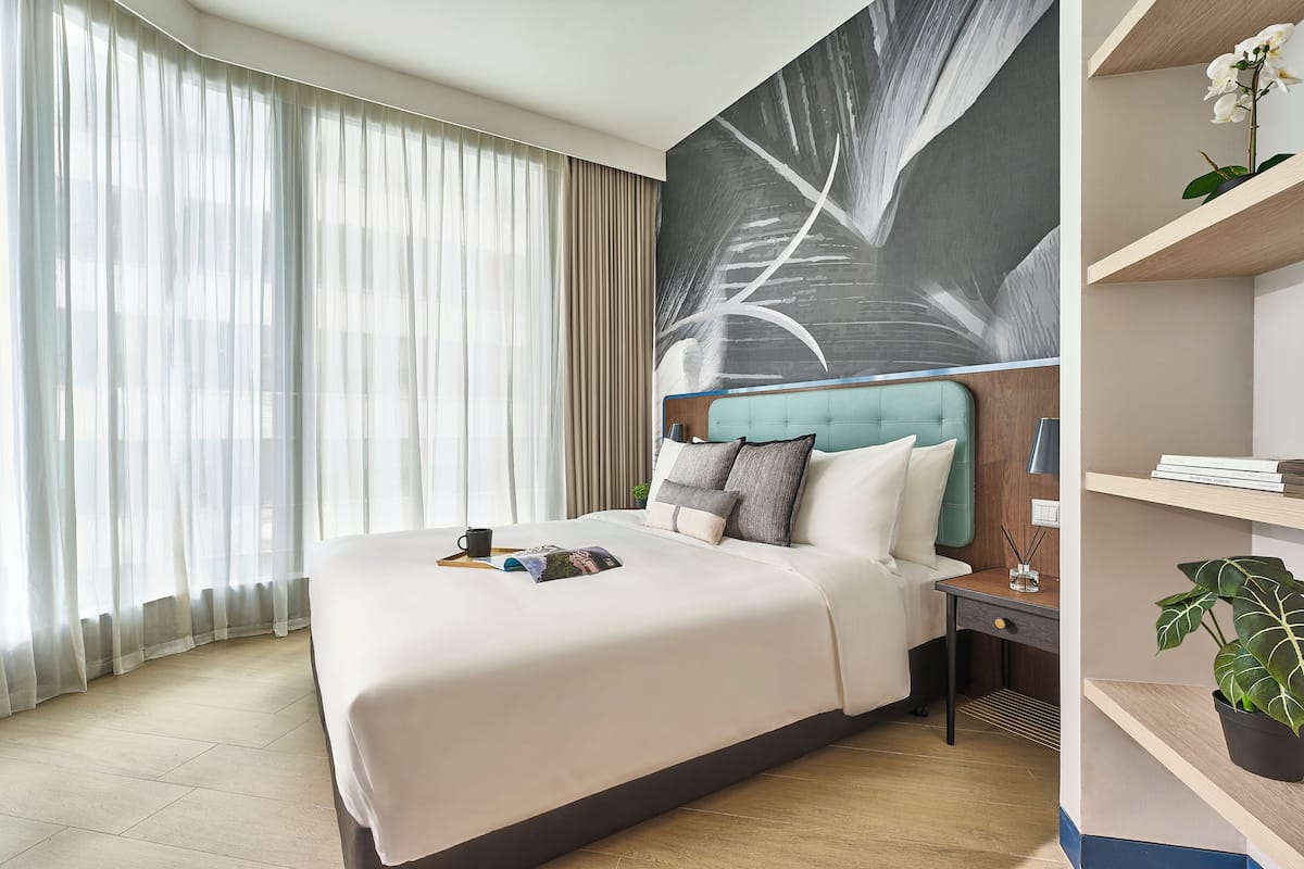 Una habitación de hotel con una cama grande, una mesita de noche, un escritorio y un estante en la pared con una planta.