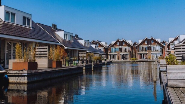 Ein Wohngebiet an einem Kanal mit modernen Häusern, einem Holzsteg und blauem Himmel.
