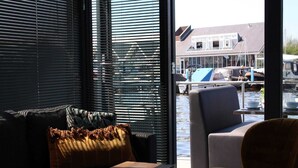 Ein modernes Interieur mit einer Couch, einem Sessel und einem kleinen Tisch. Ein großes Fenster bietet Blick auf eine Marina mit Booten.