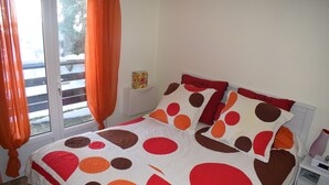 A bed with a polka dot and solid color quilt, a white nightstand, and a window with curtains.