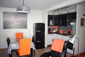 Cucina compatta con frigorifero, fornello e microonde. È presente un tavolo da pranzo con sedie e una lampada a sospensione sopra.