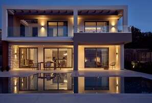 A modern two-story house with a glass pool, outdoor seating, and a stone facade.