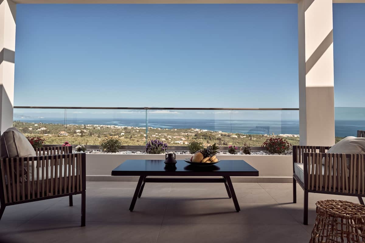 A balcony with a table, two chairs, and a view of the sea and landscape.
