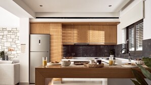 A modern kitchen with wooden cabinets, a stainless steel refrigerator, and a dining area with a round rug. - Julieta Villas (Zakynthos)