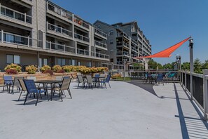 An outdoor patio area with tables and chairs, surrounded by a low fence and a red shade sail.