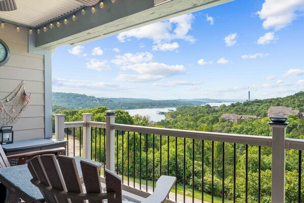 A balcony with a view of a river and hills, furnished with chairs and a table.