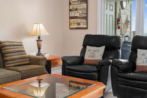 A living room with a sofa, two armchairs, a coffee table, and a lamp. There is a sign on the wall with family rules.